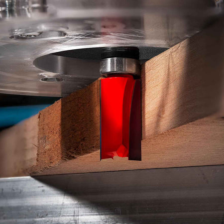 A close-up action shot of the Freud 50-101 router bit in use, showing the top-mounted pilot bearing following a template to precisely trim the edge of a thick hardwood board.