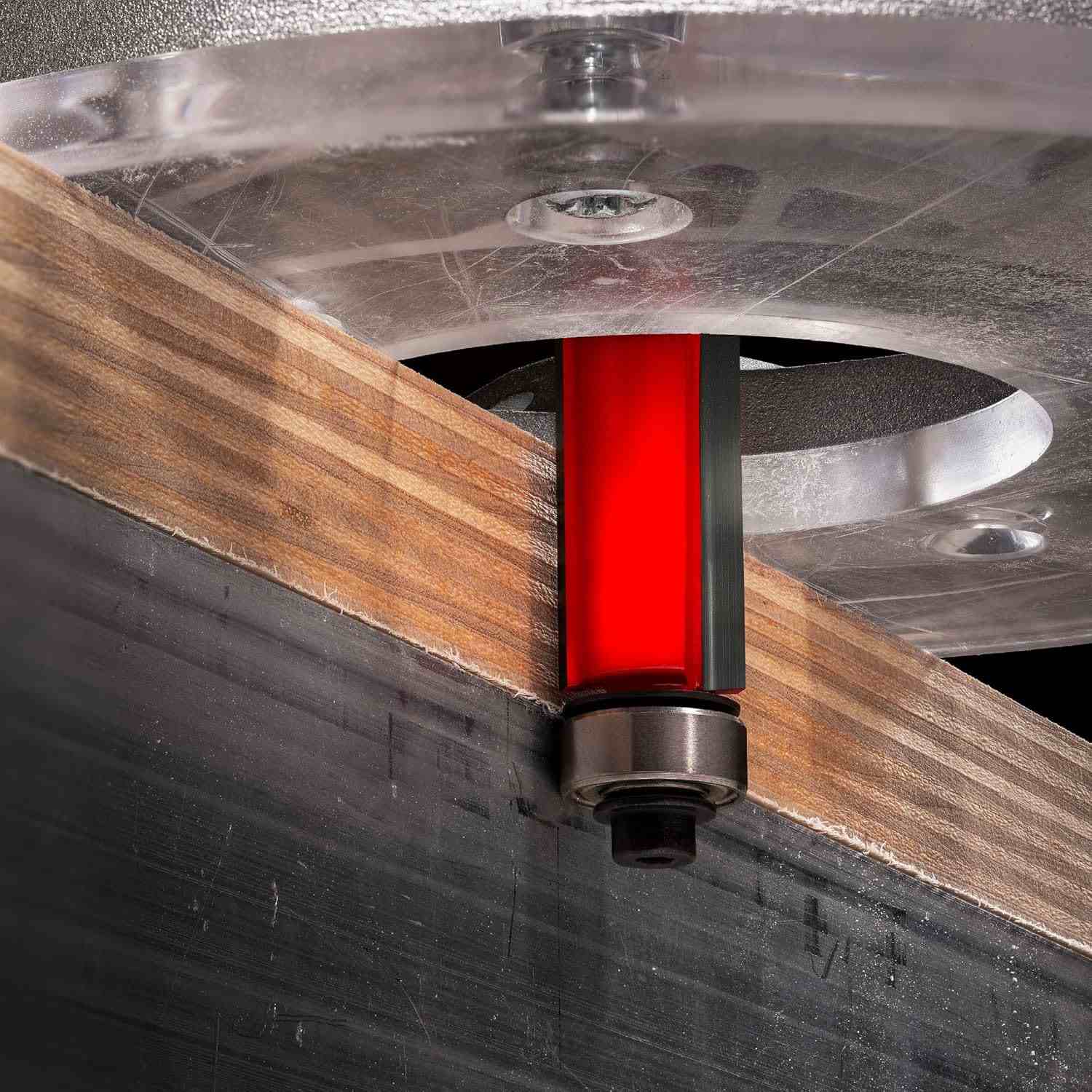 Close-up action shot of the Freud 50-509 bearing flush trim bit mounted in a router, actively trimming a plywood edge perfectly flush with the bottom ball bearing pilot.