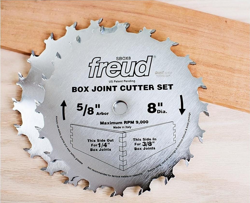 Lifestyle image of the Freud 8-inch box joint cutter blades resting on a piece of hardwood, demonstrating the professional industrial design and rotation direction for woodworking.