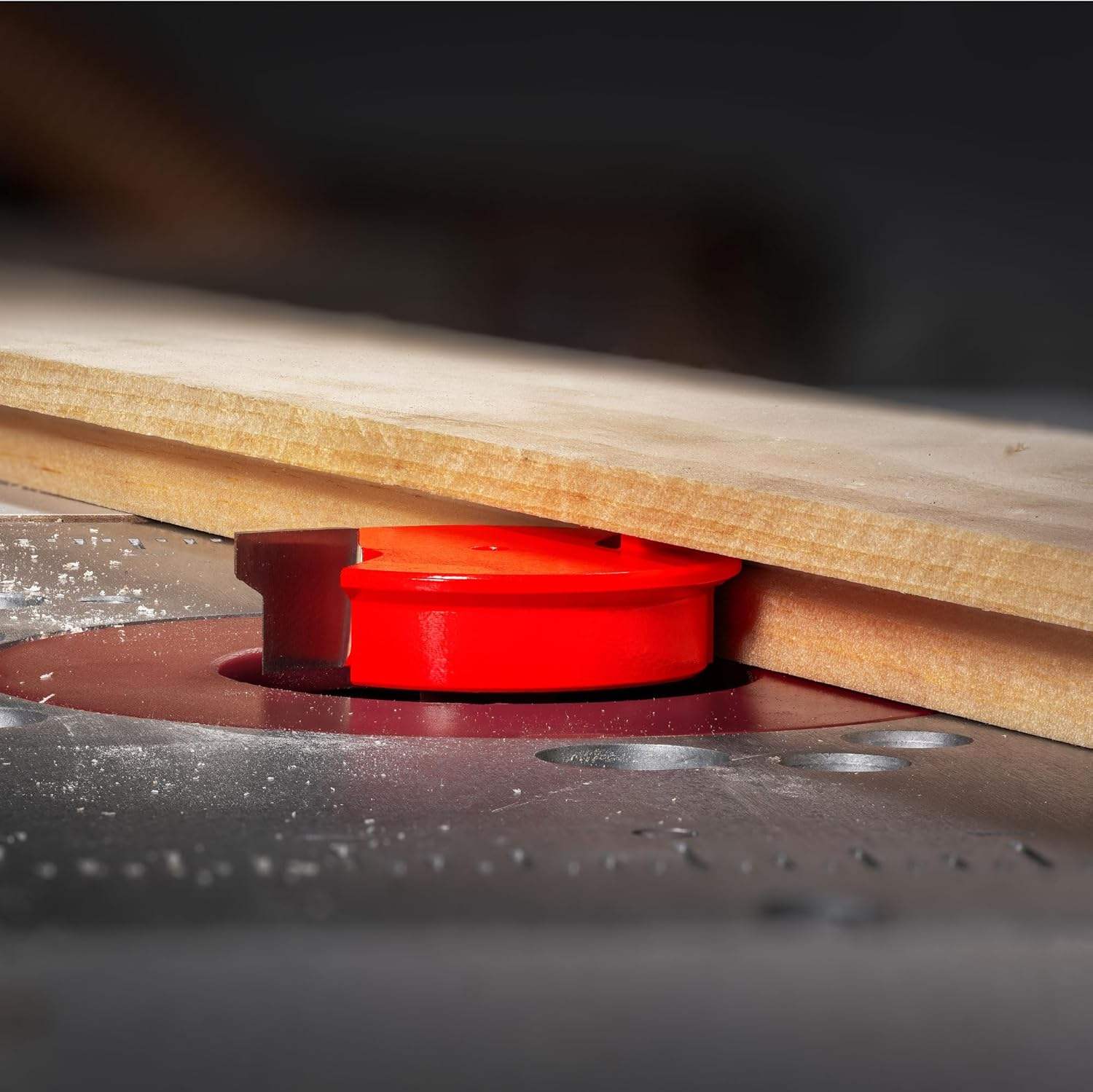 Close-up action shot of the Freud 99-240 bit mounted in a router table, cutting a profile into the edge of a wood board.