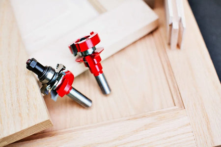 Close-up lifestyle shot of the two red Freud 99-863 adjustable rail and stile router bits resting on a beautifully crafted custom wood cabinet door.