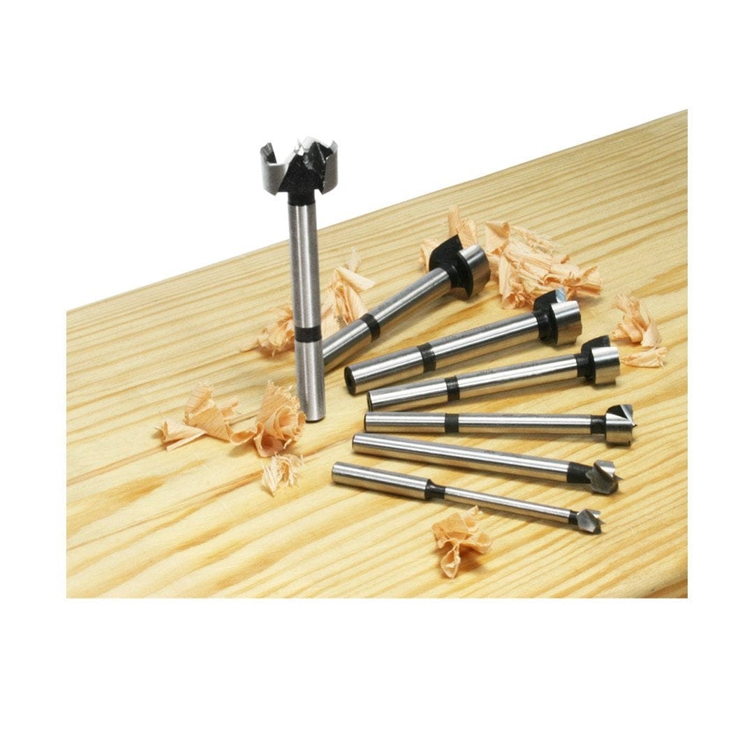 A group shot of the seven Freud precision shear Forstner bits resting on a light-colored wood board with fresh wood curls, demonstrating efficient chip removal and industrial quality.