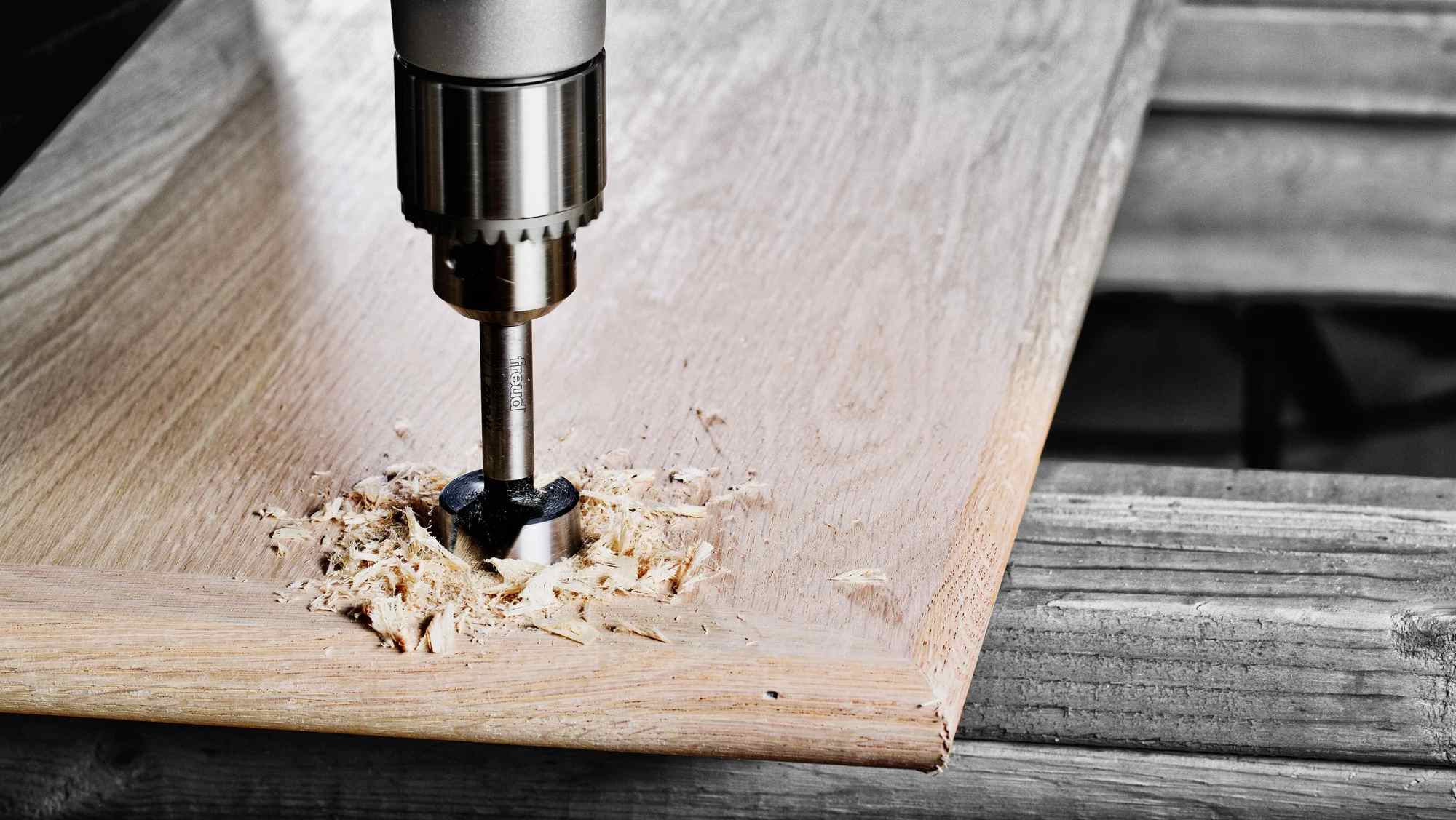 An overhead action shot of a Freud Forstner bit drilling a clean, splinter-free hole into a hardwood board, demonstrating the precision of the serrated edge and smooth flat-bottom finish.