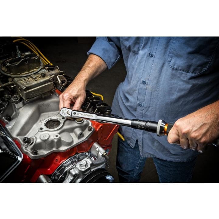 Mechanic using a GEARWRENCH torque wrench to tighten a bolt on a red V8 engine block, demonstrating precision torque application during engine assembly.