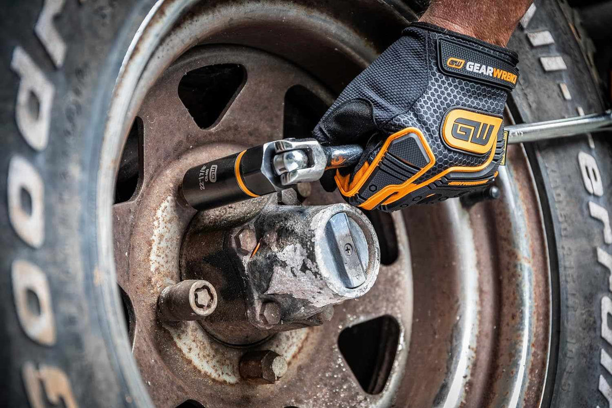 A mechanic using a hand ratchet with a Bolt Biter extraction socket attached to work on a damaged fastener on a rusty vehicle hub.