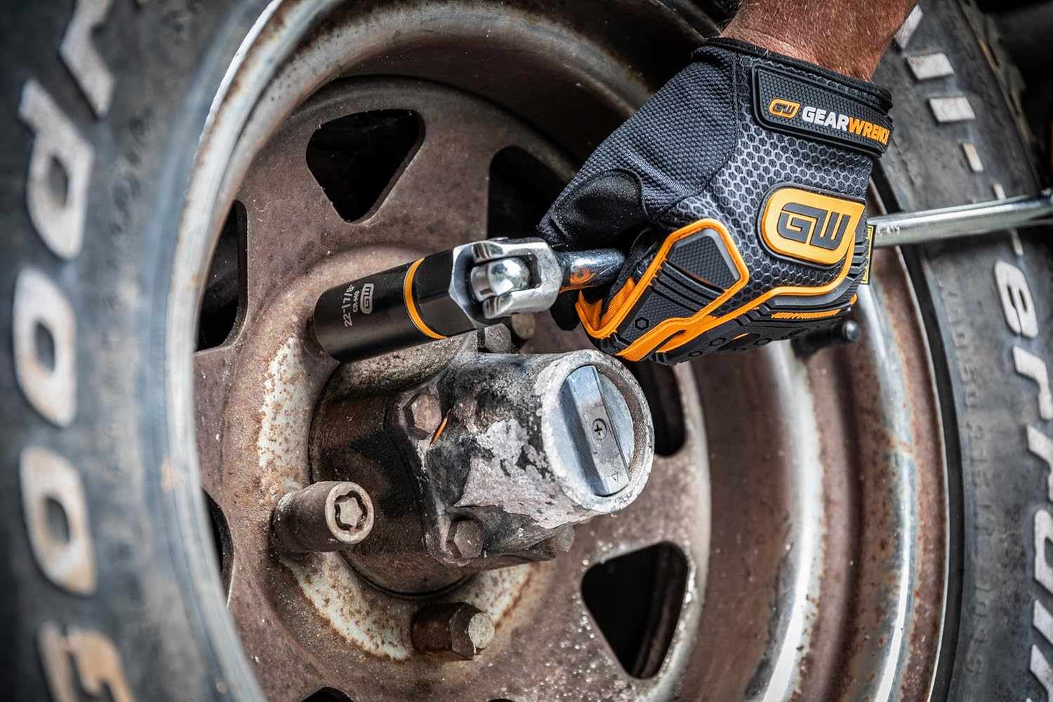 A mechanic using a hand ratchet with a Bolt Biter extraction socket attached to work on a damaged fastener on a rusty vehicle hub.