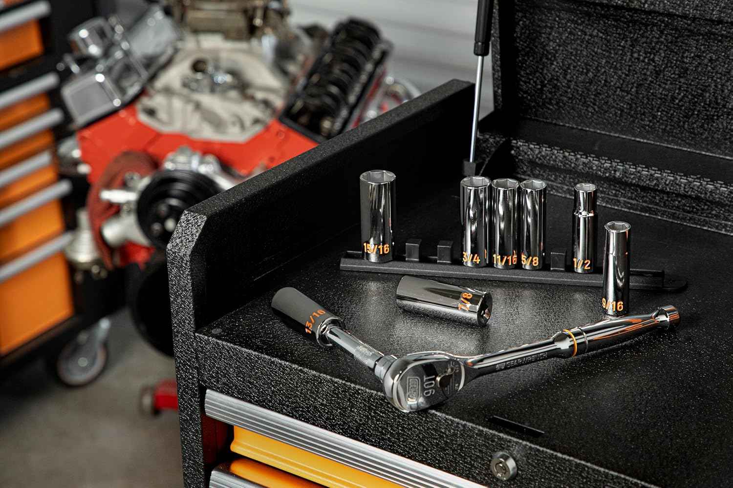 An authentic workshop view of GEARWRENCH deep chrome sockets standing on an orange organizer rail next to a 90-tooth teardrop ratchet handle on top of a black tool cabinet slider tray.