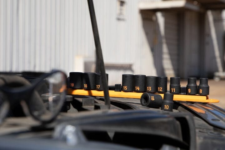 An action photo of the GEARWRENCH 12-piece metric Hi-Viz impact socket set on its orange rail sitting on a vehicle engine, illustrating the tool set's use in professional mechanical maintenance.