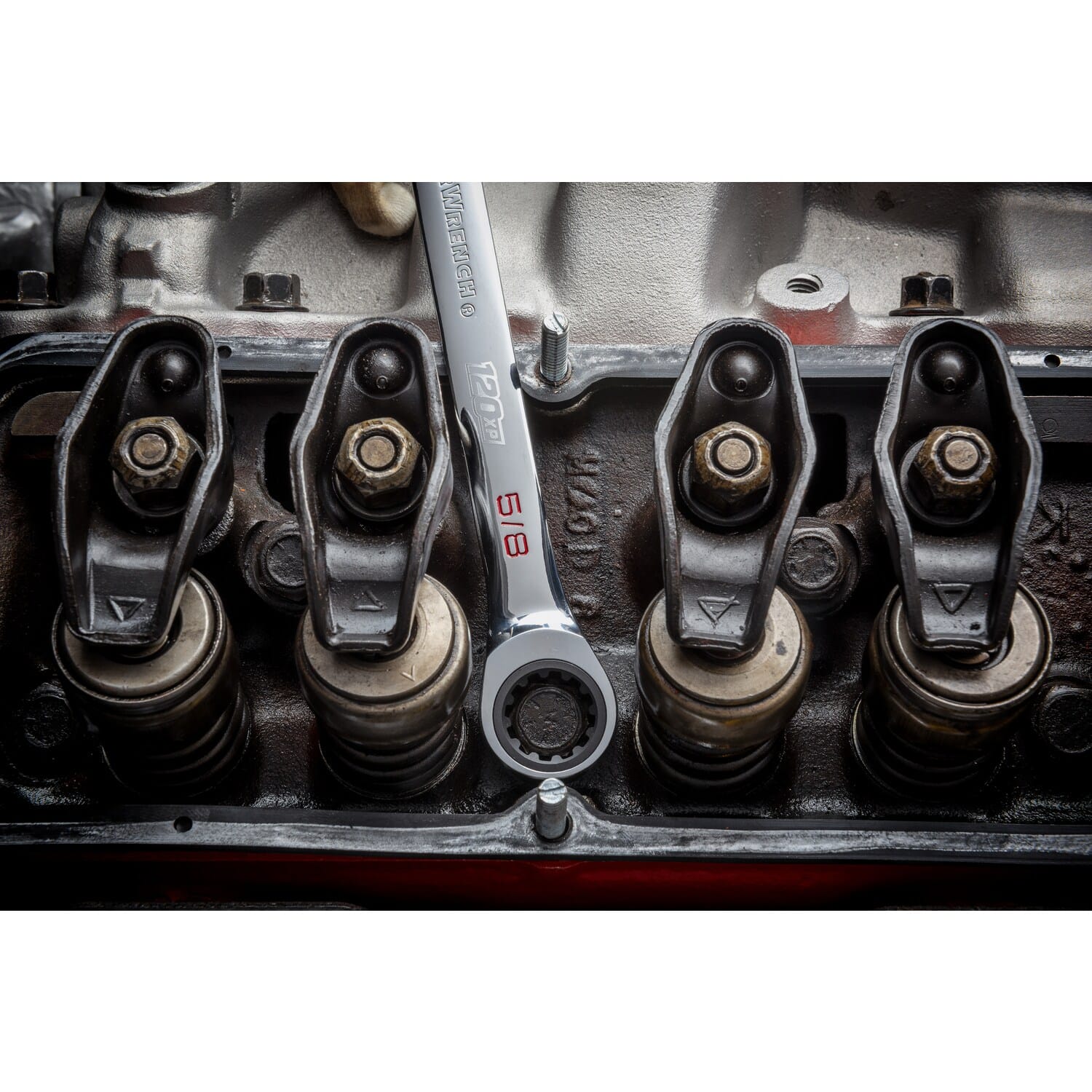 An overhead detail shot of a technician using a 5/8 inch GEARWRENCH 120XP XL ratcheting wrench, with the open end engaged on a rocker arm bolt inside an opened high-performance V8 engine block.
