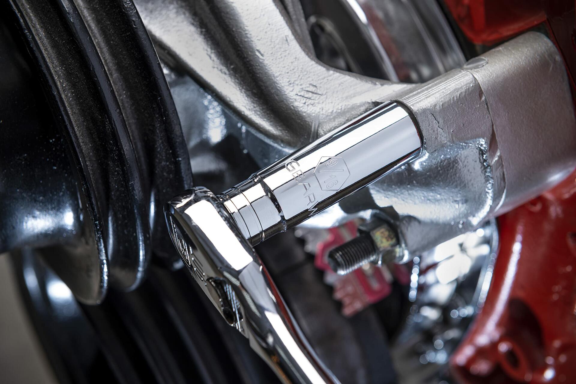 A close-up action shot of a GEARWRENCH 13mm chrome socket and ratchet being used to tighten a bolt on a vehicle's shiny silver brake caliper assembly.