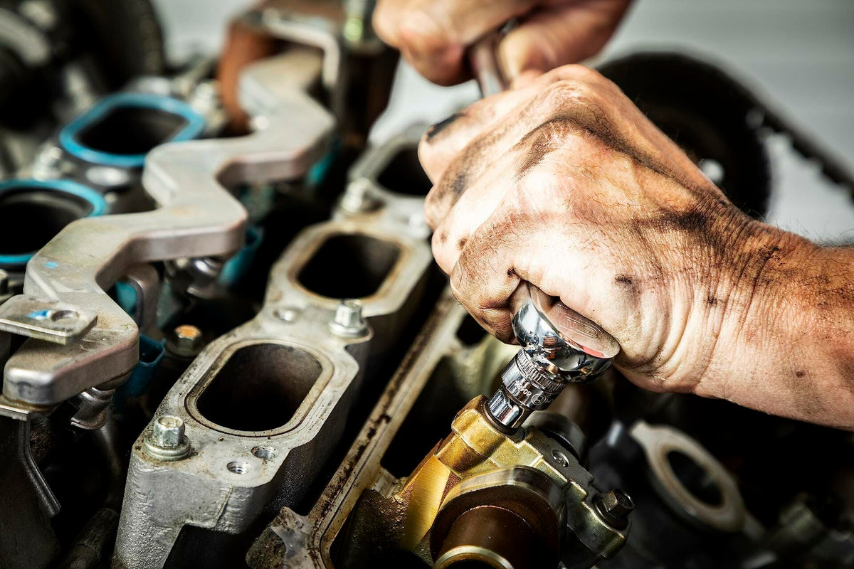 A mechanic's hands using a GEARWRENCH ratchet and socket to tighten a bolt on a complex engine block.