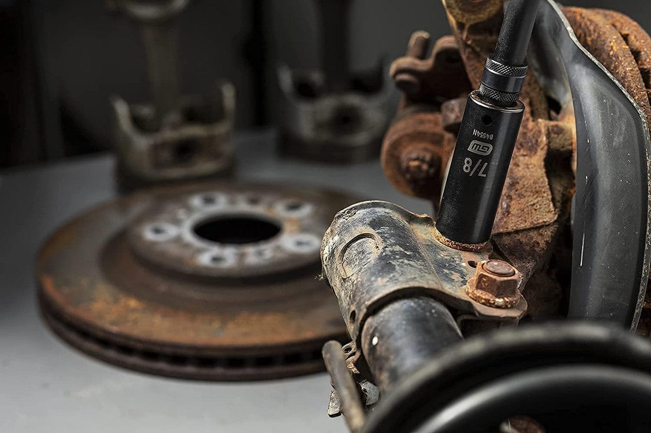 The GEARWRENCH 7/8-inch deep impact socket (84554N) is shown attached to an extension, removing a rusty bolt from an automotive steering knuckle.