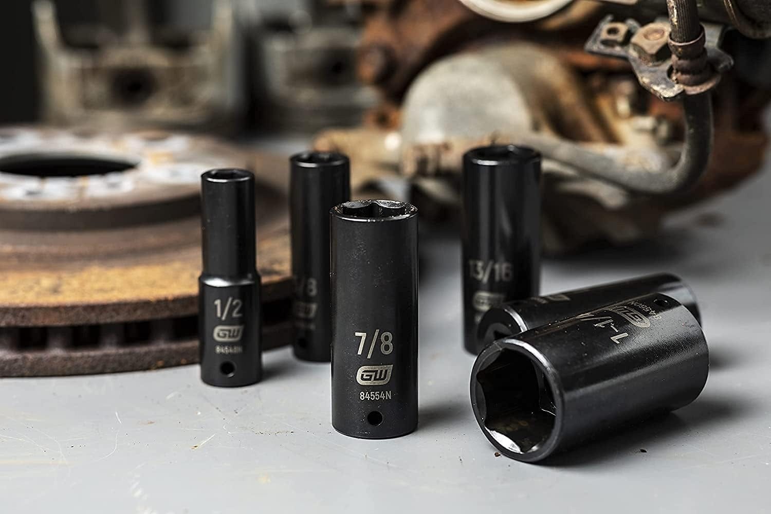A group of GEARWRENCH 1/2-inch drive deep impact sockets, including 1/2-inch and 7/8-inch sizes, resting on a workbench next to a rusty brake rotor.