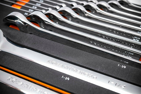 GEARWRENCH chrome combination wrenches arranged in foam tray; sizes including 1 inch, 1-1/8 inch, and 1-1/4 inch visible with branding on wrench shafts.