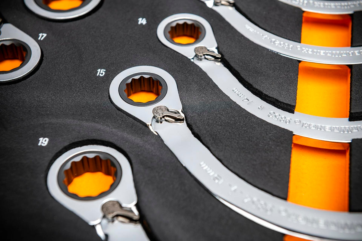 Close-up of ratcheting box-end wrenches in a foam tray labeled with metric sizes including 14, 15, 17, and 19; chrome finish and 12-point ratcheting ends visible against black and orange foam.