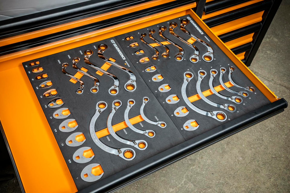 Drawer of a tool chest containing ratcheting wrenches organized in a black foam insert with orange accents; each slot labeled by size and securely holding polished chrome wrenches