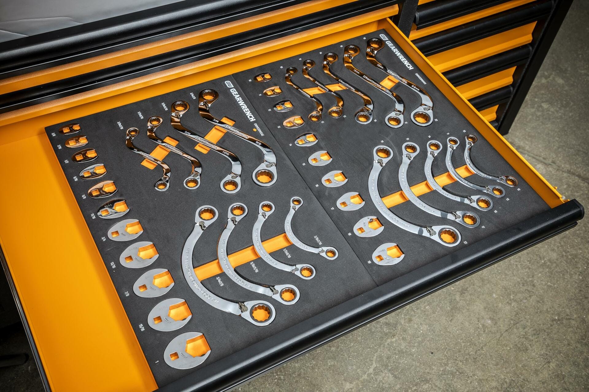 Drawer of a tool chest containing ratcheting wrenches organized in a black foam insert with orange accents; each slot labeled by size and securely holding polished chrome wrenches