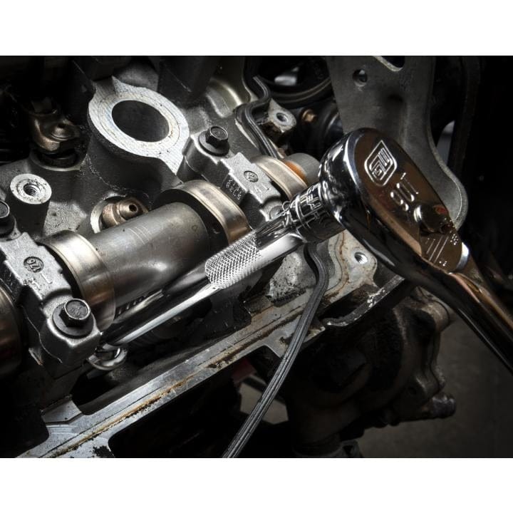 A mechanic using a chrome 90-tooth GEARWRENCH ratchet and an extension to work on a bolt on an open car engine, demonstrating precise access in a tight area.