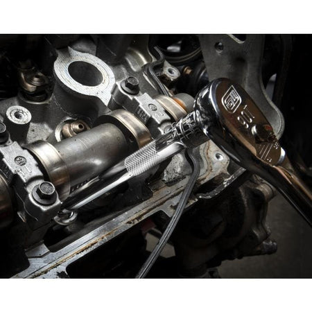 A mechanic using a chrome 90-tooth GEARWRENCH ratchet and an extension to work on a bolt on an open car engine, demonstrating precise access in a tight area.