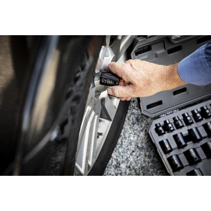 An action shot of a hand taking a 22mm impact socket from the open case, which is resting on the ground next to a car tire.