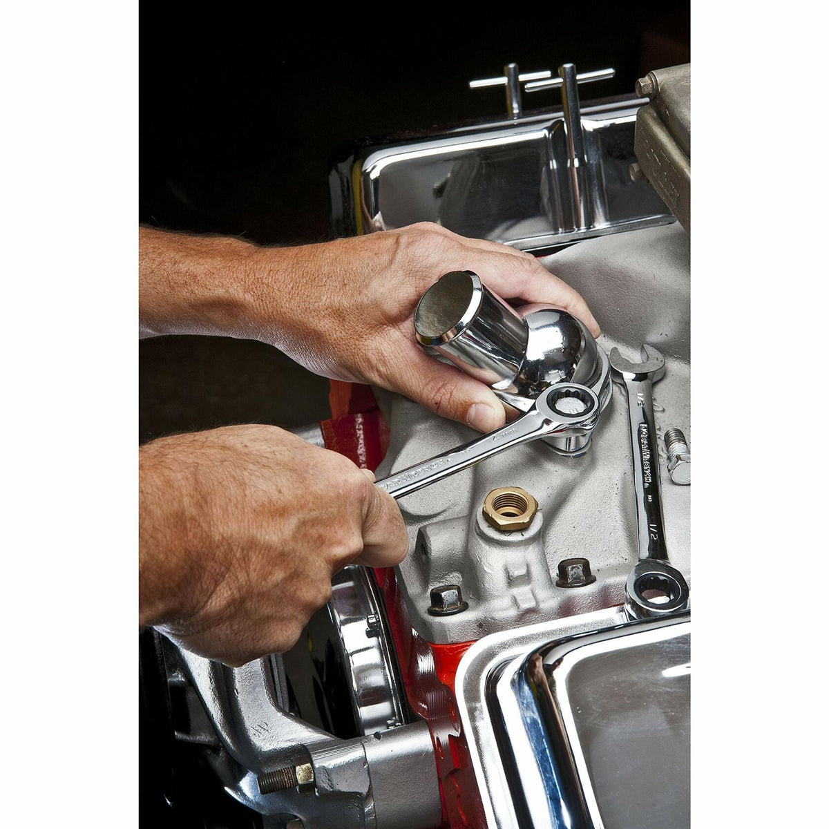 Hands gripping a wrench and socket while working on a clean, chrome-finished engine component during automotive assembly or repair.