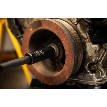A GEARWRENCH 18mm deep impact socket (84576N) attached to an extension bar, inserted into the central bolt of a rusty engine crankshaft pulley.