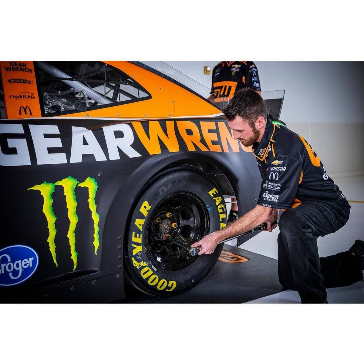 A professional mechanic using the GEARWRENCH 85065M heavy-duty torque wrench to tighten lug nuts on a NASCAR stock car, demonstrating its precision in high-performance automotive racing environments.