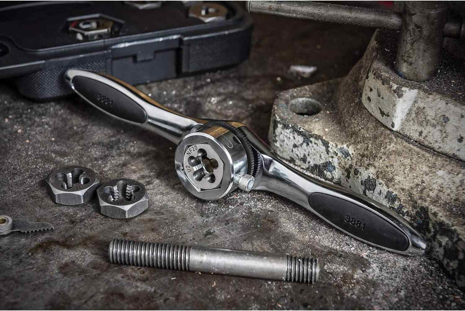 Lifestyle shot of the GearWrench ratcheting T-handle and hex dies on a metal workbench next to a vise, demonstrating its use in cleaning up damaged threads on a large steel bolt.