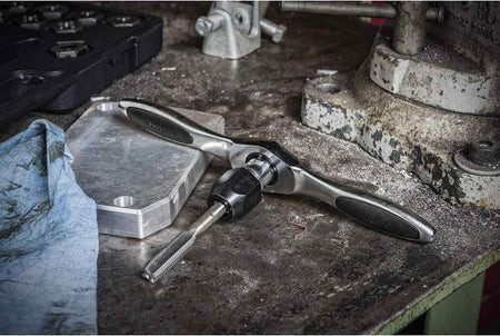 Action shot of a professional technician using the GearWrench ratcheting tap and die set to cut internal metric threads in a metal plate, showcasing the tool's leverage and control.