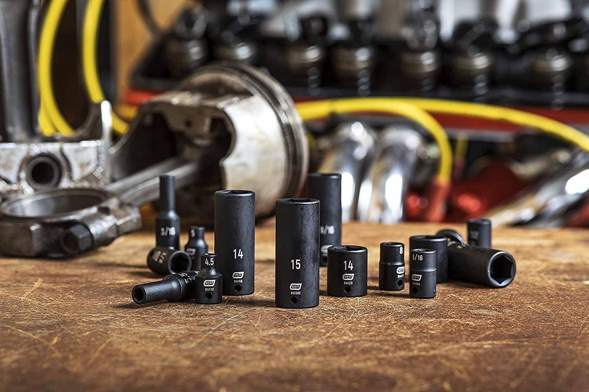 A collection of GEARWRENCH 3/8-inch drive impact sockets, including 14mm, 15mm, and 5/16-inch sizes, resting on a workbench surrounded by engine components.