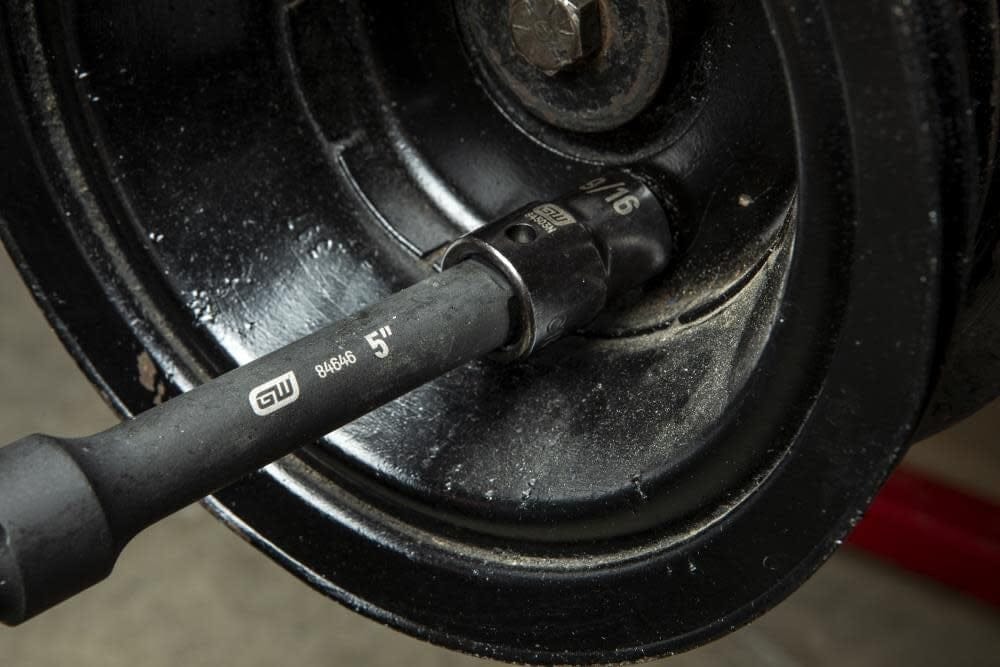 An action photo of a GEARWRENCH 1/2 inch drive 5-inch impact extension bar and socket being used to reach a recessed fastener on a black industrial pulley system.