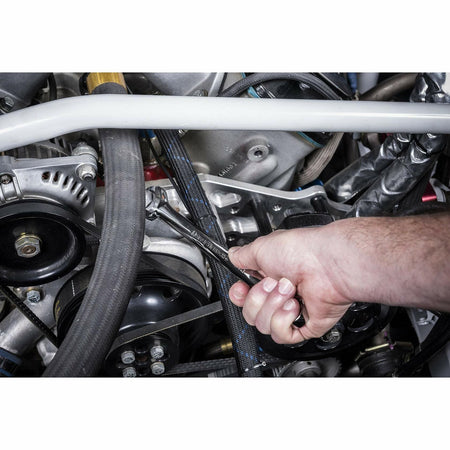 Close-up of a hand using a wrench to adjust a component in a car engine bay. The wrench is applied to the serpentine belt system near pulleys and hoses, illustrating real-world use of a combination wrench in automotive maintenance.