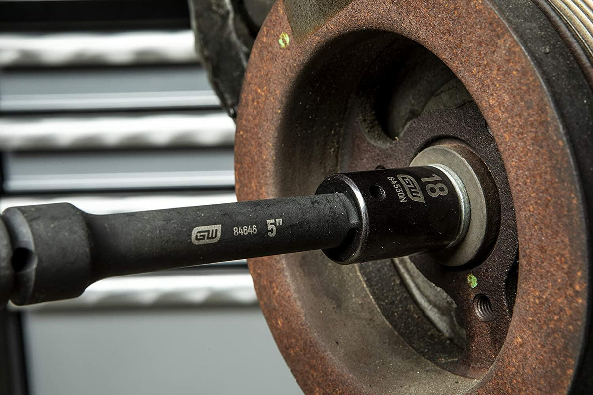 Close-up of an 18mm impact socket attached to a 5-inch extension bar being used on a rusted automotive component. Demonstrates tool use in tight or recessed areas during mechanical repair.
