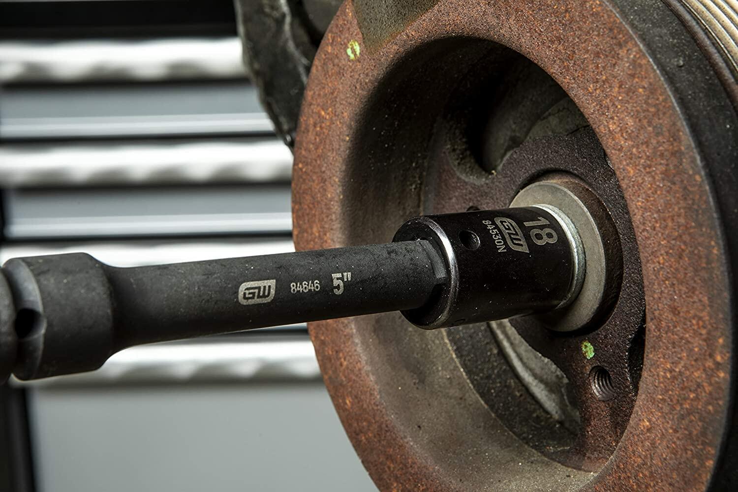 Close-up of an 18mm impact socket attached to a 5-inch extension bar being used on a rusted automotive component. Demonstrates tool use in tight or recessed areas during mechanical repair.