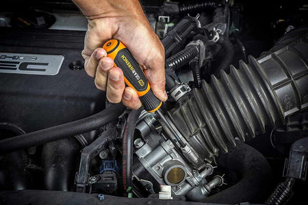 An action photo of a technician using a GEARWRENCH Phillips screwdriver to adjust a component inside a high-performance engine bay, demonstrating the tool's professional utility and ergonomic grip.
