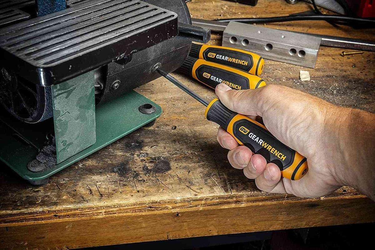 A professional using a GEARWRENCH slotted screwdriver to perform maintenance on a piece of machinery on a wooden workbench, showcasing the tool's precision and comfort in a shop setting.