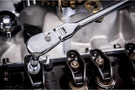 An action photo of a technician using a GEARWRENCH 90-tooth flex head ratchet to access a bolt inside a high-performance engine, demonstrating the tool's specialized utility in cramped mechanical environments.