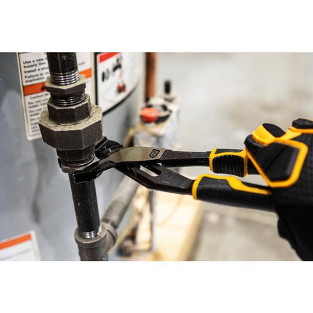 Close-up action shot of the GEARWRENCH 8-inch PITBULL pliers tightening a plumbing hex nut on a black iron pipe, showcasing the aggressive biting power of the V-Jaw design.