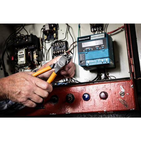 An electrician using the GEARWRENCH diagonal cutting pliers to precisely trim heavy-gauge wire inside a professional electrical control panel.