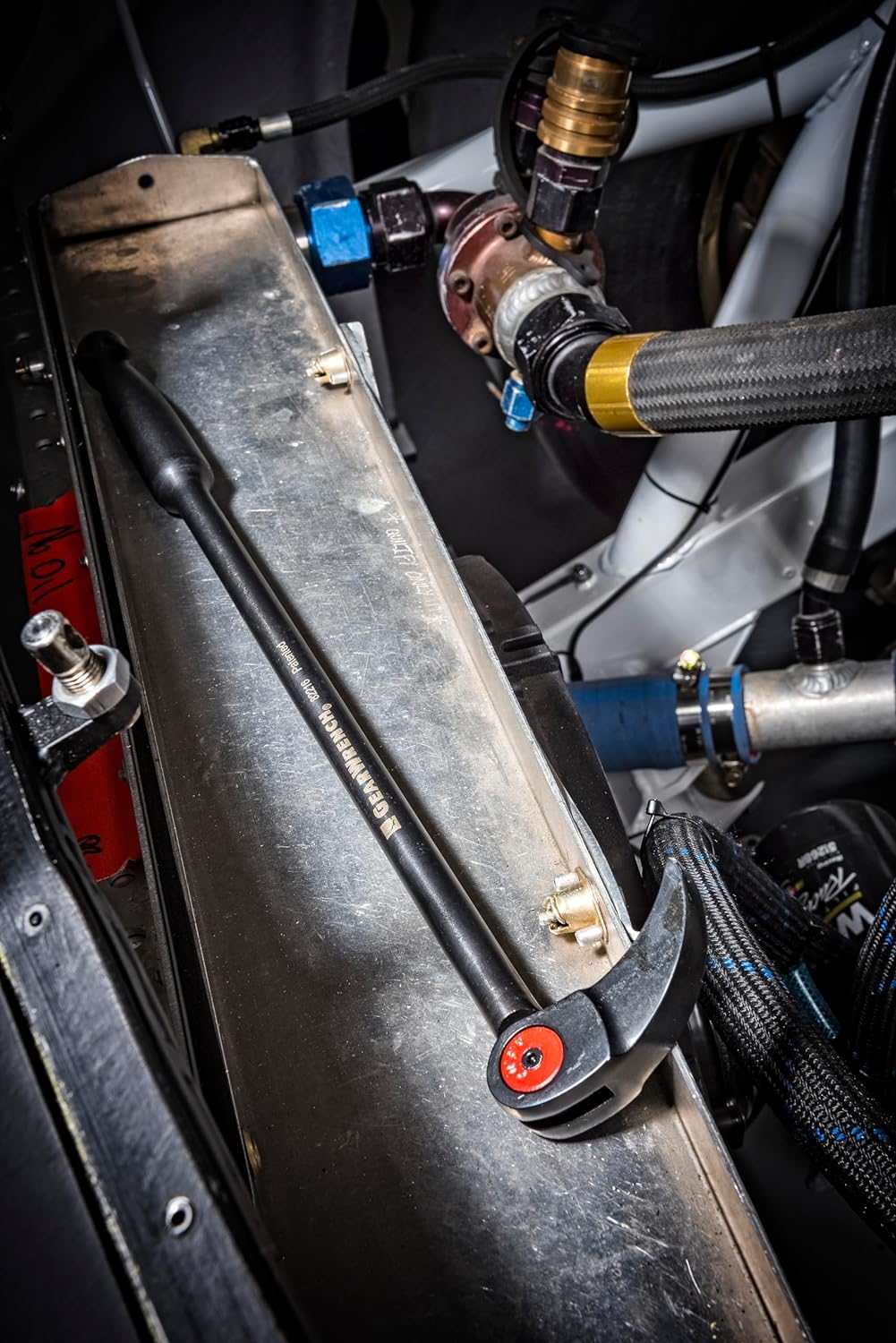 An action photo of the GEARWRENCH indexing pry bar resting on a metal component within a complex industrial engine assembly, demonstrating the tool's compact size and professional utility in a workshop environment.