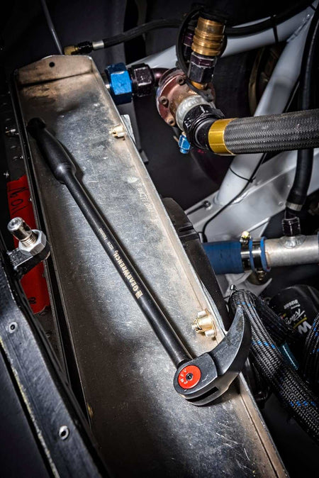 An action photo of the GEARWRENCH indexing pry bar resting on a metal component within a complex industrial engine assembly, demonstrating the tool's compact size and professional utility in a workshop environment.