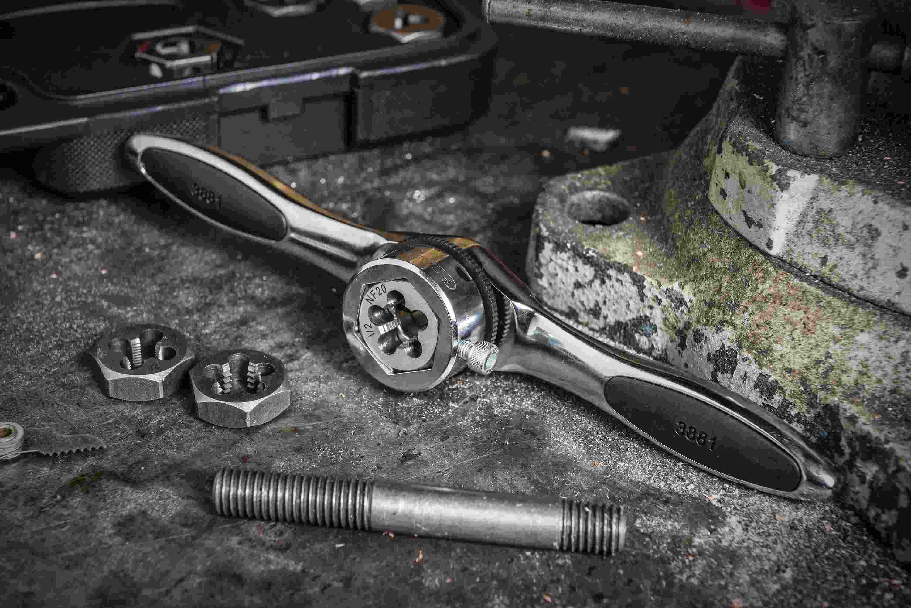 Close-up of the GEARWRENCH ratcheting T-handle and hex die being used on a workbench to re-thread a steel bolt, demonstrating the 5-degree swing arc in a real-world application.