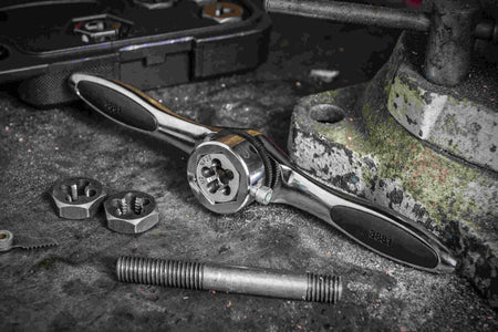 Close-up of the GEARWRENCH ratcheting T-handle and hex die being used on a workbench to re-thread a steel bolt, demonstrating the 5-degree swing arc in a real-world application.
