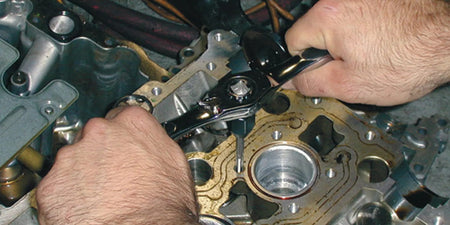 Action shot of a professional technician using the GEARWRENCH ratcheting T-handle and tap to repair internal threads on an aluminum engine block in a mechanical workshop.