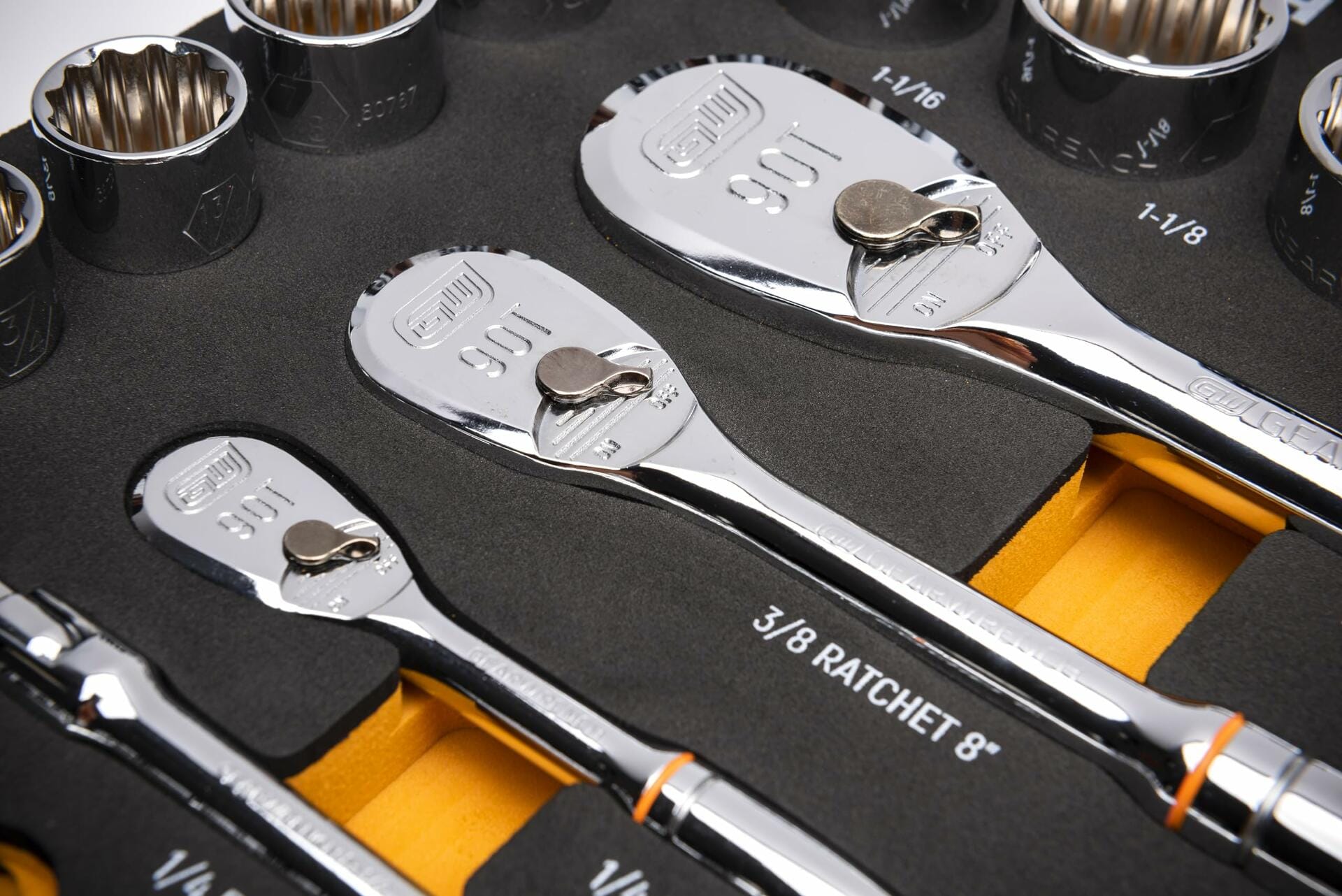 Close-up of ratchets and sockets in a foam tray. Includes 3/8" drive 90T ratchet and fractional inch sockets such as 1", 1-1/16", and 1-1/8". Each tool is secured in a labeled cutout with a yellow contrast layer beneath the foam for visibility.