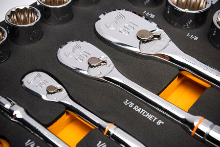 Close-up of ratchets and sockets in a foam tray. Includes 3/8" drive 90T ratchet and fractional inch sockets such as 1", 1-1/16", and 1-1/8". Each tool is secured in a labeled cutout with a yellow contrast layer beneath the foam for visibility.