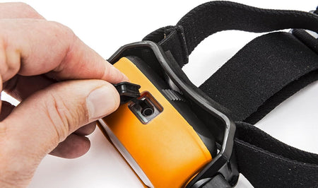 A close-up action shot of a hand opening the protective rubber port cover on the GEARWRENCH headlamp to access the mini DC charging input for the lithium-ion battery.