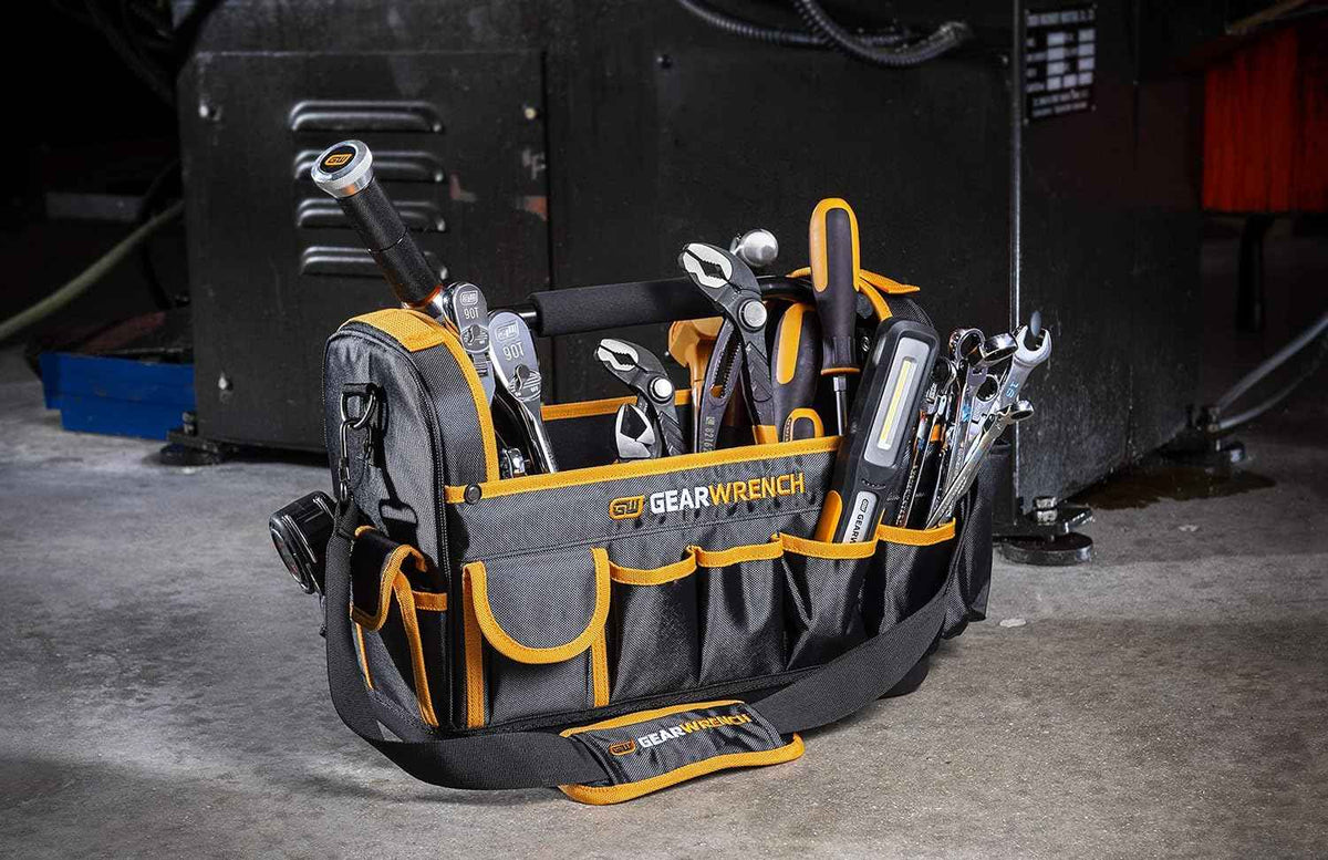 The GEARWRENCH 83146 16-inch tool tote bag fully loaded with professional hand tools, including ratchets, pliers, and a work light, standing on a concrete shop floor to demonstrate stability.