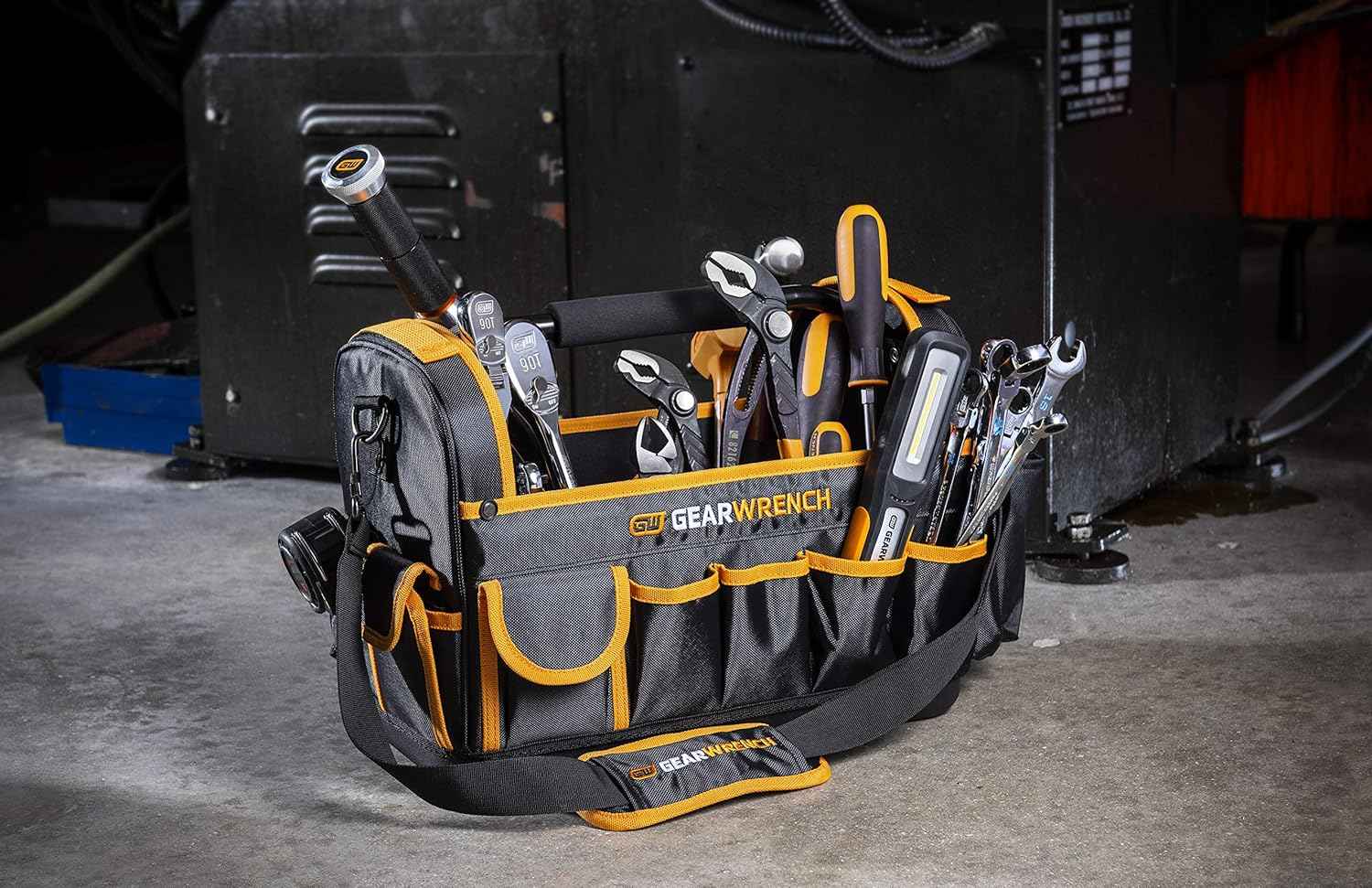 The GEARWRENCH 83146 16-inch tool tote bag fully loaded with professional hand tools, including ratchets, pliers, and a work light, standing on a concrete shop floor to demonstrate stability.