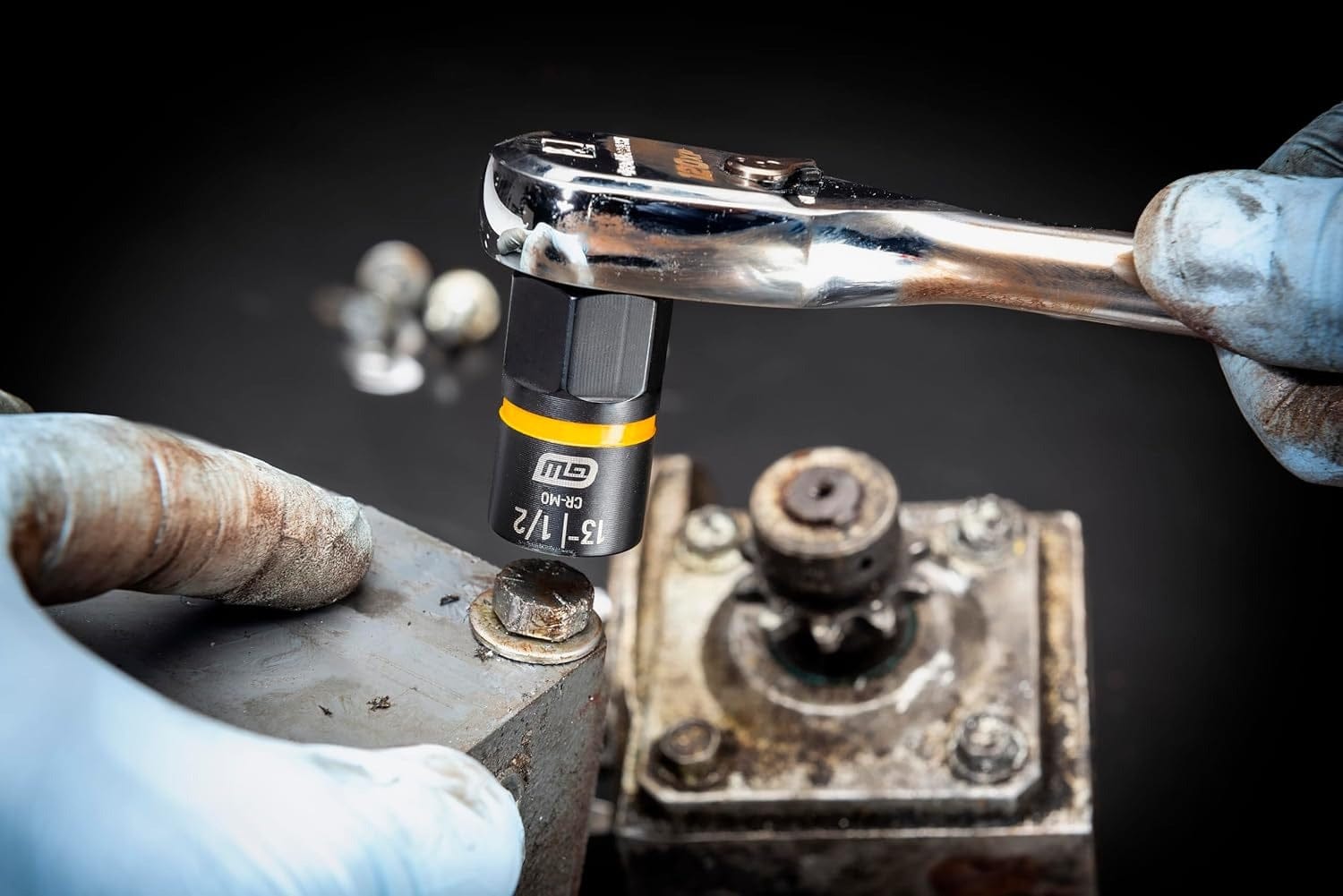 A gloved hand uses a ratchet with a GEARWRENCH Bolt Biter socket to grip and remove a rounded, rusty bolt from a piece of machinery.
